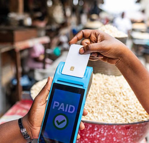 Contactless payment success, customer makes a transaction with a credit card via blue point of sale, POS terminal in a bustling outdoor African local traditional corn grains market.